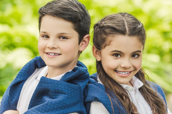 Close-up portrait of kids in white shirts and jumpers over shoulders with crossed arms looking at camera — Stock Photo