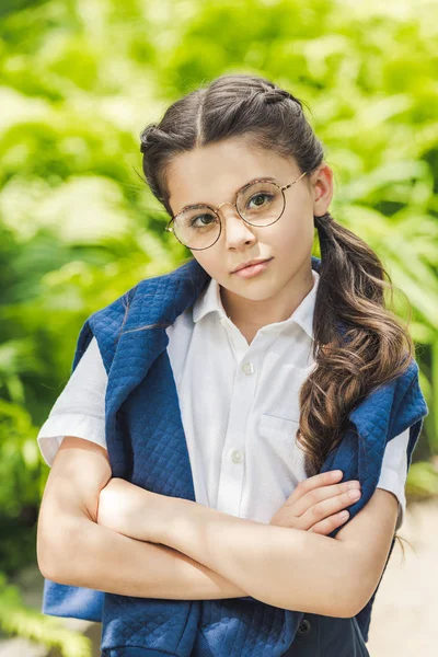 Serious schoolgirl with crossed arms in white shirt and jumper over shoulders looking at camera — Stock Photo