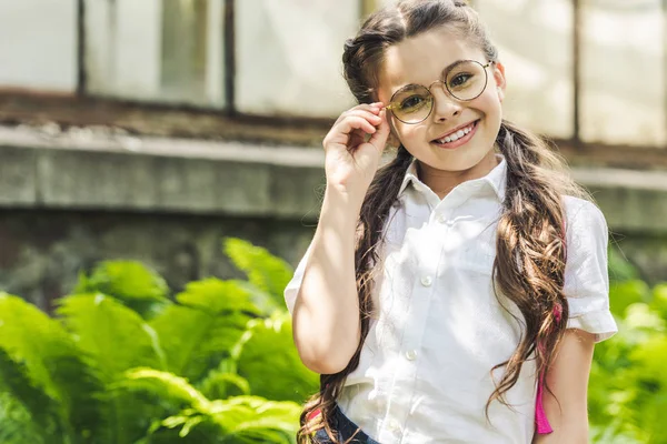 Schöne Schülerin in Uniform und Brille, die im Park in die Kamera schaut — Stockfoto