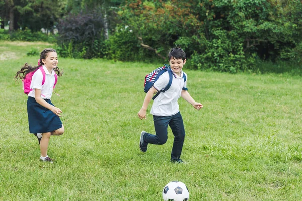 Schüler mit Rucksäcken spielen gemeinsam Fußball auf Wiese im Park — Stockfoto