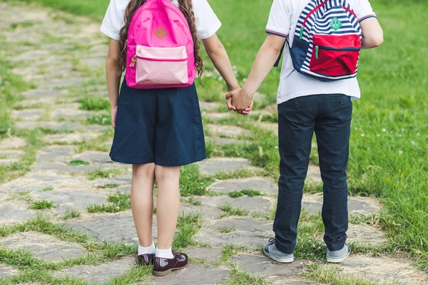 Tiro recortado de escolares caminando por el camino en el parque y tomados de la mano - foto de stock