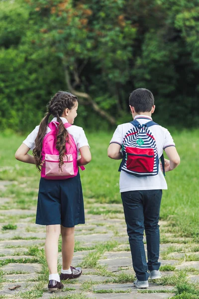 Rückansicht von entzückenden Schulkindern, die gemeinsam auf dem Gehweg im Park spazieren — Stockfoto