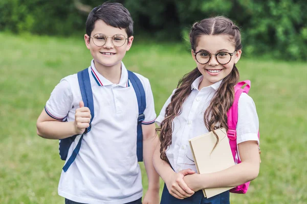 Glückliche Schulkinder mit Brille blicken auf Wiese im Park in die Kamera — Stockfoto