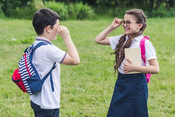 Adorable schoolchildren with backpacks looking at each other through eyeglasses — Stock Photo