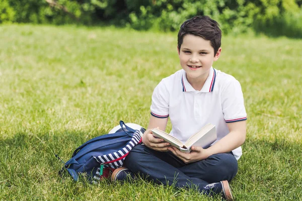 Feliz niño leyendo libro mientras está sentado en la hierba - foto de stock