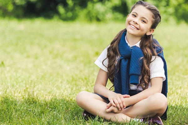 Красивая дошкольница, сидящая на траве в парке — стоковое фото
