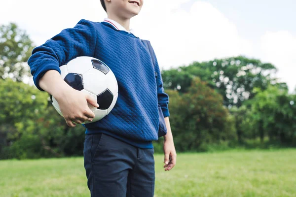 Tiro recortado de niño sosteniendo pelota de fútbol en el campo de hierba - foto de stock
