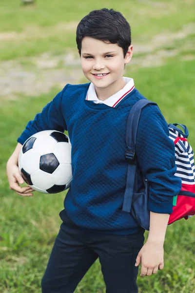 Милий хлопець з футбольним м'ячем з футбольним м'ячем і рюкзаком на трав'яному полі — стокове фото