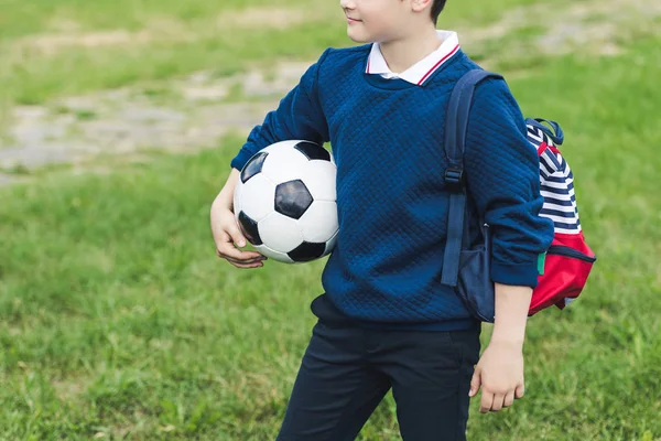 Tiro cortado de criança com bola de futebol com bola de futebol e mochila no campo de grama — Fotografia de Stock
