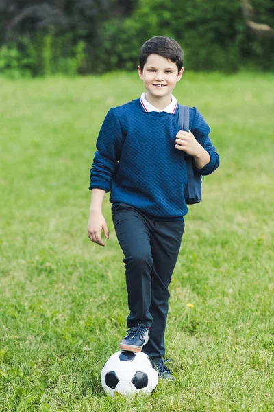 Adorable kid with soccer ball and backpack on grass field — Stock Photo