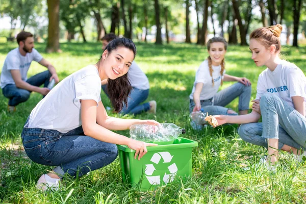 Young smiling volunteers cleaning park with recycling box — Stock Photo