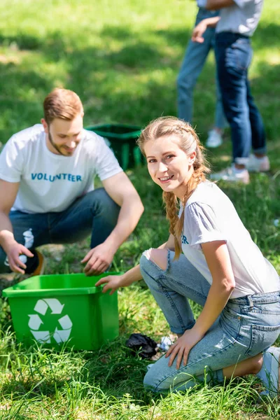 Ein paar lächelnde Freiwillige reinigen Rasen mit Recyclingbox — Stockfoto