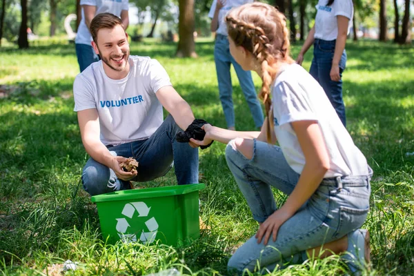 Voluntarios felices limpieza de césped con caja de reciclaje verde - foto de stock