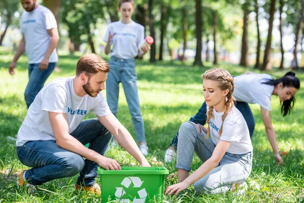 Молодые волонтеры чистят газоны с зеленой коробкой для переработки — стоковое фото