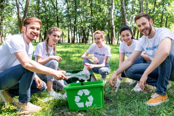 Giovani volontari con green recycling box cleaning park — Foto stock