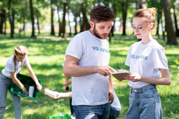 Coppia guardando il libro di testo mentre i volontari pulizia parco — Foto stock