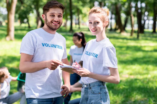 Coppia sorridente in possesso di libro di testo mentre i volontari pulizia parco — Foto stock