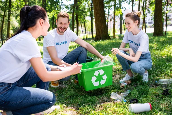 Jóvenes voluntarios sonrientes con caja de reciclaje verde en el parque - foto de stock