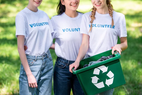 Cropped view of young female volunteers with green recycling box — Stock Photo