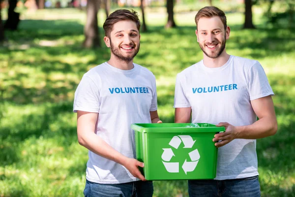 Jovens voluntários do sexo masculino com caixa de reciclagem verde — Fotografia de Stock