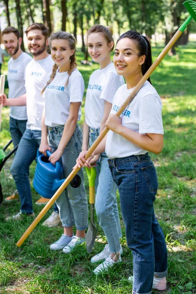 Jóvenes voluntarios sonrientes de pie en el parque - foto de stock