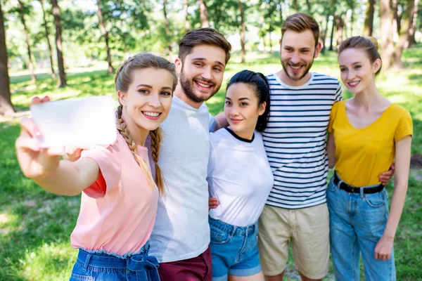 Jóvenes amigos sonrientes tomando selfie en smartphone en el parque - foto de stock