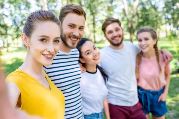 Jóvenes amigos felices tomando selfie juntos en parque - foto de stock