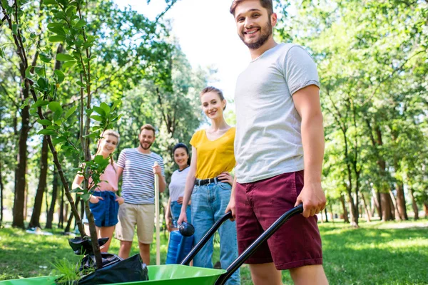 Jeunes amis avec brouette et nouveaux arbres faisant du bénévolat dans le parc — Photo de stock