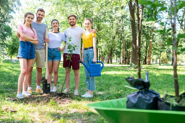 Young friends with watering can and shovel planting new trees in park — Stock Photo