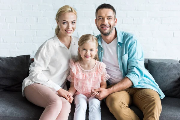 Счастливая семья улыбается на камеру, сидя вместе на диване дома — стоковое фото