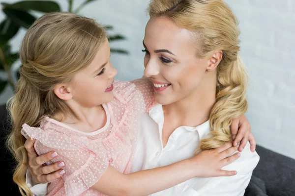 Schöne glückliche Mutter und Tochter umarmen und lächeln einander zu Hause — Stockfoto