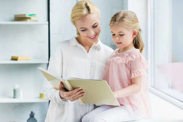 Bela mãe feliz e filha ler livro juntos em casa — Fotografia de Stock