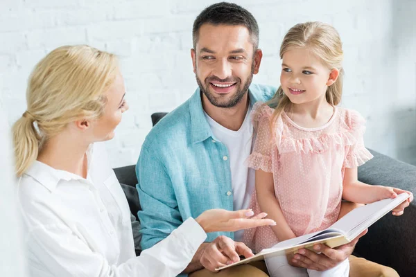 Happy parents with cute little daughter reading book together at home — Stock Photo