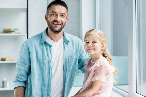 Glücklicher Vater und entzückende kleine Tochter lächeln zu Hause gemeinsam in die Kamera — Stockfoto