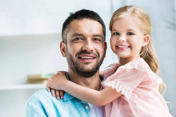 Feliz padre e hija abrazando y sonriendo a la cámara - foto de stock