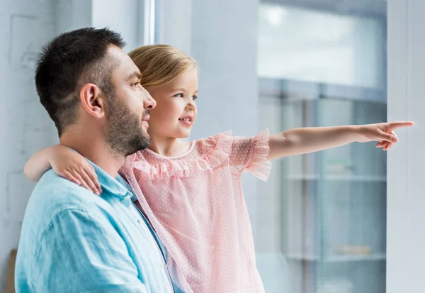 Father and cute smiling daughter looking away while child pointing with finger — Stock Photo