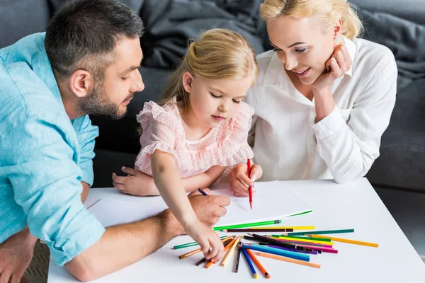 Vista de ángulo alto de la familia con un niño dibujo con lápices de colores juntos en casa - foto de stock