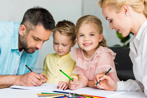 Parents heureux avec de mignons petits enfants dessinant ensemble à la maison — Photo de stock