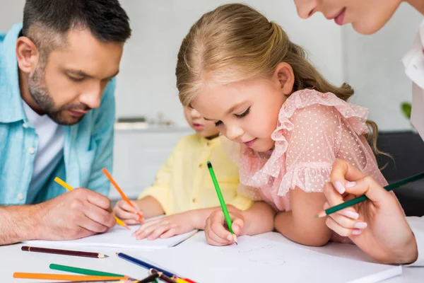 Cropped shot of parents with cute little children drawing with colored pencils at home — Stock Photo