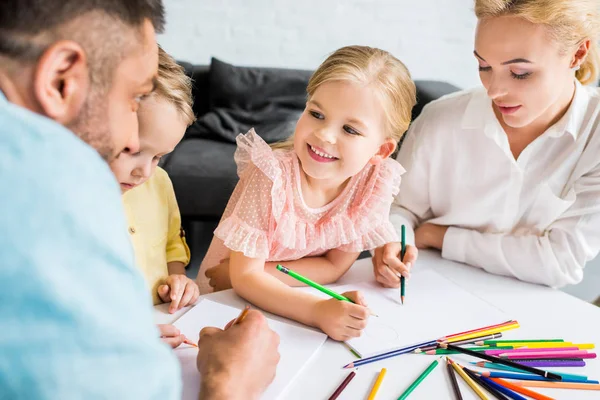 Щаслива сім'я з двома дітьми малює кольоровими олівцями вдома — стокове фото