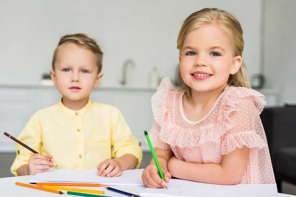 Lindos niños pequeños dibujando y sonriendo a la cámara en casa - foto de stock