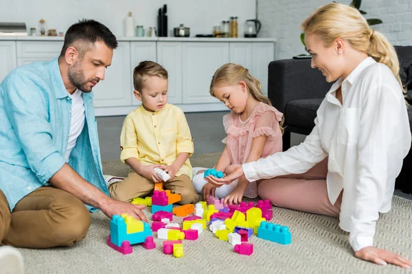 Familie mit zwei Kindern sitzt auf Teppich und spielt mit bunten Blöcken — Stockfoto