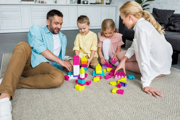 Família feliz com duas crianças brincando com blocos coloridos em casa — Fotografia de Stock