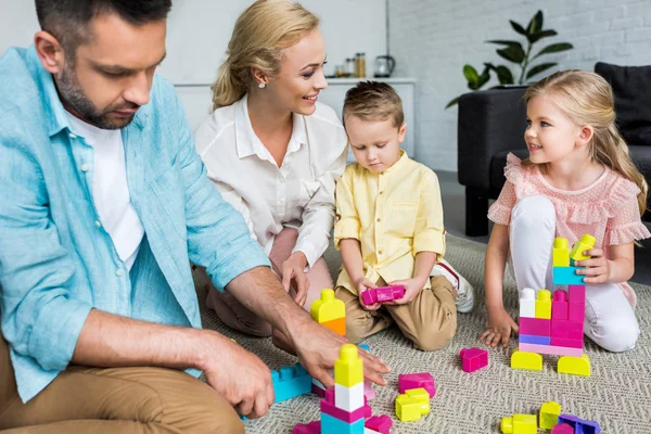 Счастливая семья с двумя детьми, играющая дома с разноцветными блоками — стоковое фото