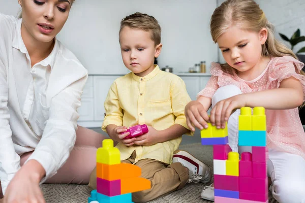 Plan recadré de la mère avec de mignons petits enfants jouant avec des blocs colorés à la maison — Photo de stock