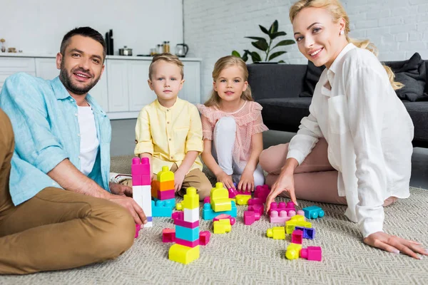 Щаслива сім'я посміхається на камеру, граючи з барвистими блоками вдома — стокове фото