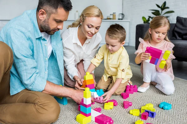 Pais com crianças adoráveis brincando com blocos coloridos em casa — Fotografia de Stock