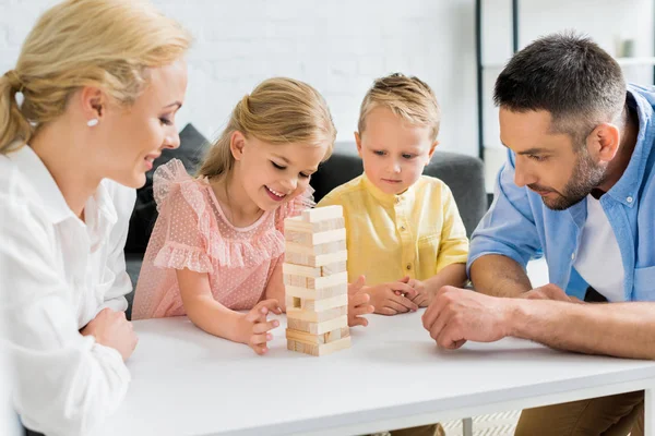 Щаслива сім'я з двома дітьми, які грають з дерев'яними блоками вдома — стокове фото