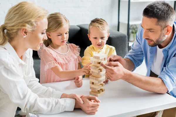 Famille avec deux enfants construisant tour à partir de blocs de bois à la maison — Photo de stock