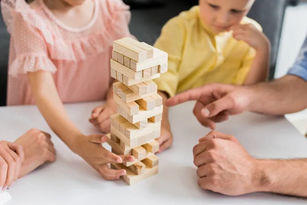 Colpo ritagliato di famiglia con due bambini torre di costruzione da blocchi di legno a casa — Foto stock